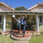 A photo of Amanda Kerr standing in front of a house that she just sold.